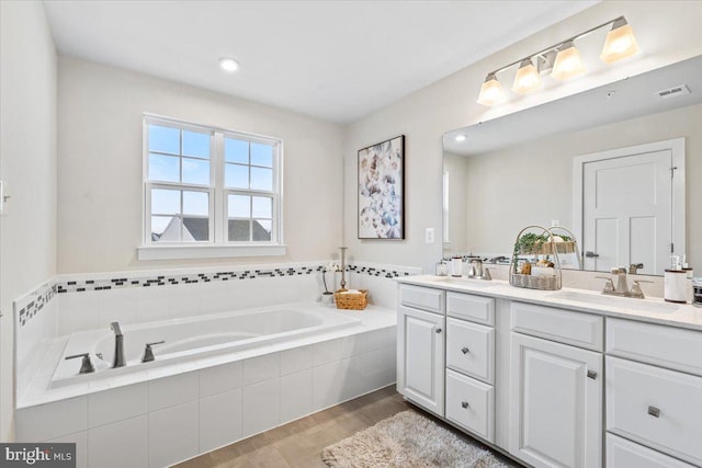 bathroom featuring a relaxing tiled tub, wood-type flooring, and vanity