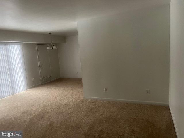 carpeted empty room featuring an inviting chandelier