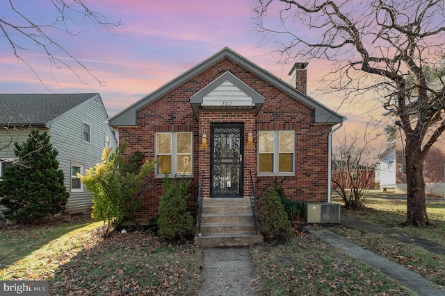 bungalow-style house with a chimney, entry steps, cooling unit, and brick siding