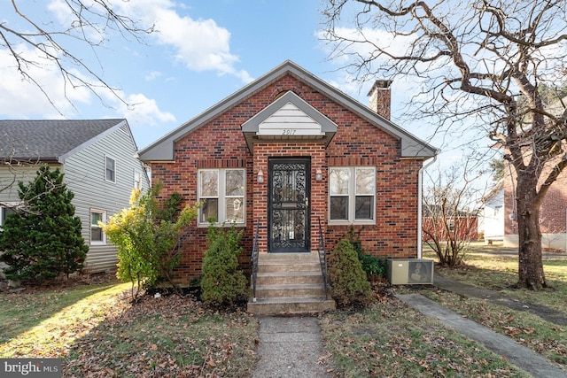 bungalow-style house with a chimney, entry steps, central AC unit, and brick siding