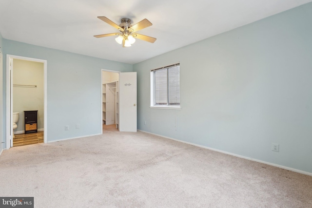 unfurnished bedroom featuring connected bathroom, a spacious closet, light carpet, a closet, and ceiling fan