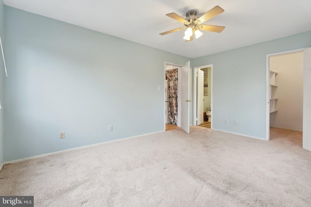 unfurnished bedroom featuring connected bathroom, a spacious closet, light colored carpet, a closet, and ceiling fan