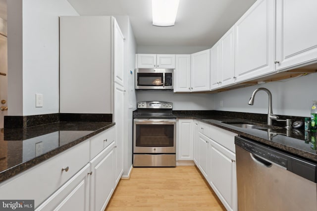 kitchen with white cabinetry, sink, stainless steel appliances, and dark stone countertops