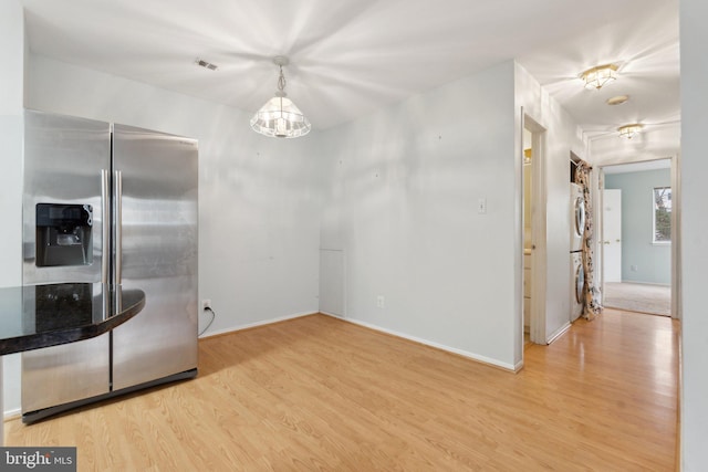 kitchen with stacked washer / drying machine, light hardwood / wood-style floors, hanging light fixtures, and stainless steel refrigerator with ice dispenser