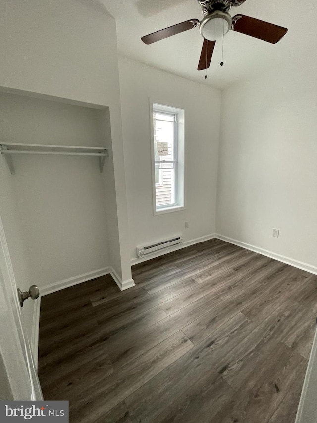 unfurnished bedroom with baseboard heating, ceiling fan, a closet, and dark wood-type flooring