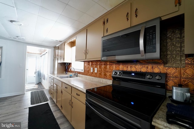 kitchen featuring black electric range oven, light wood-type flooring, decorative backsplash, sink, and cream cabinets