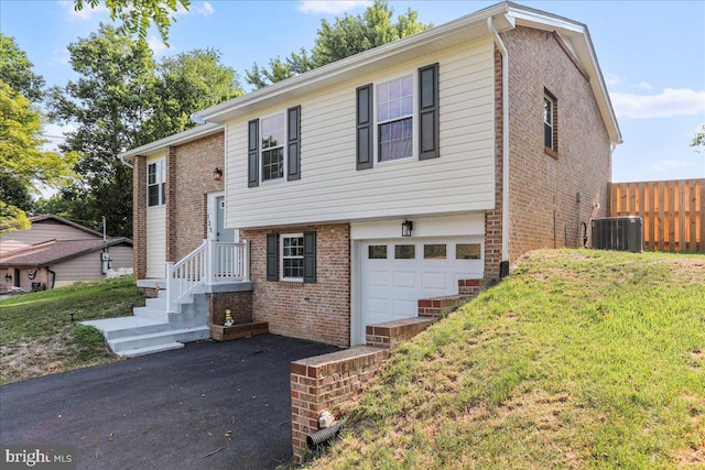 split foyer home with a front lawn, a garage, and central AC unit