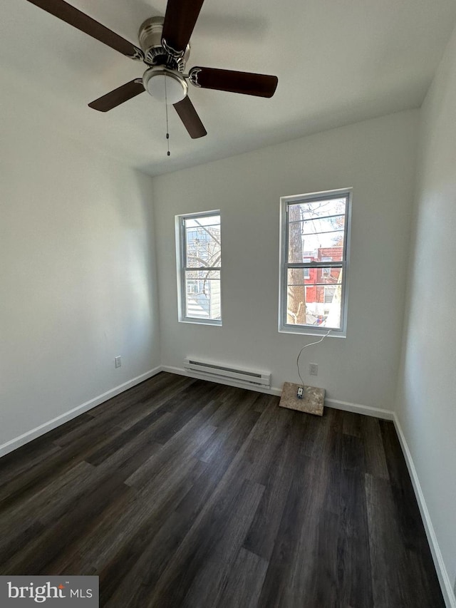 empty room featuring a healthy amount of sunlight, dark wood-type flooring, ceiling fan, and a baseboard heating unit