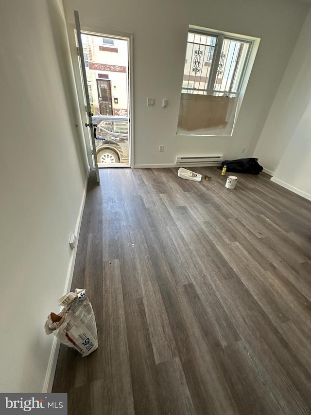 unfurnished room with dark wood-type flooring, a wealth of natural light, and a baseboard heating unit