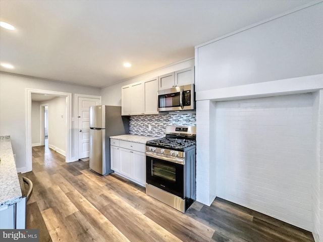 kitchen with backsplash, white cabinets, light stone countertops, appliances with stainless steel finishes, and wood-type flooring