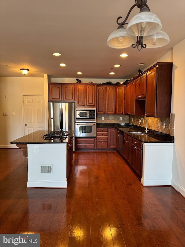 kitchen with dark hardwood / wood-style flooring, sink, decorative light fixtures, dark stone countertops, and stainless steel appliances