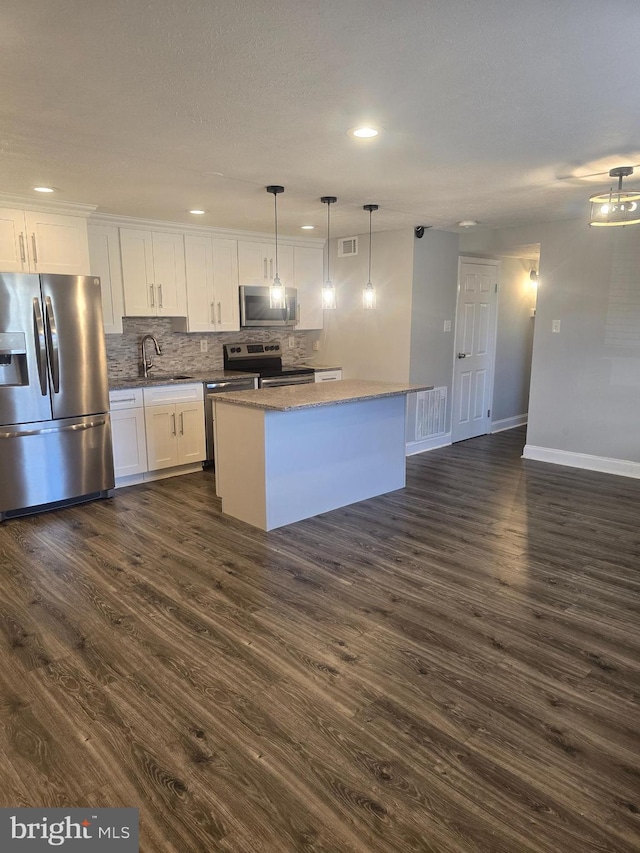 kitchen with white cabinets, sink, appliances with stainless steel finishes, decorative light fixtures, and a kitchen island