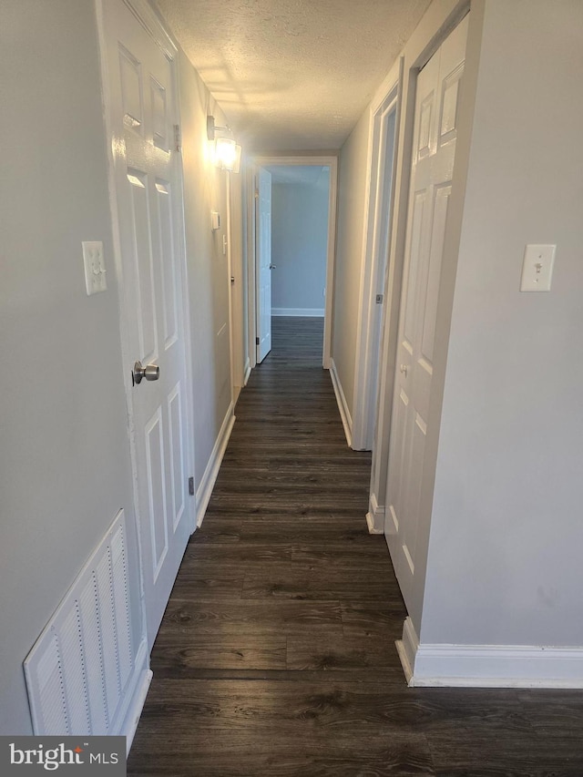 corridor with dark hardwood / wood-style floors and a textured ceiling