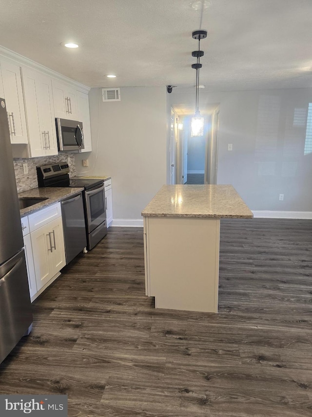 kitchen with a kitchen island, tasteful backsplash, pendant lighting, white cabinets, and appliances with stainless steel finishes