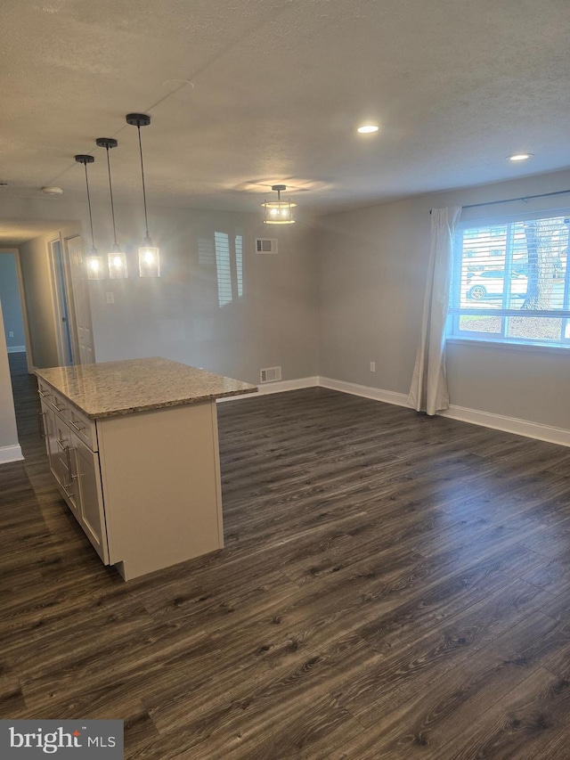 kitchen with dark hardwood / wood-style flooring, light stone countertops, a center island, and decorative light fixtures