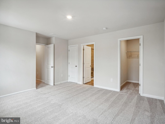 unfurnished bedroom with a walk in closet, ensuite bathroom, a closet, and light colored carpet