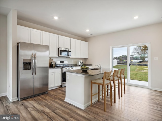 kitchen featuring dark stone counters, stainless steel appliances, a kitchen island with sink, white cabinets, and dark hardwood / wood-style floors