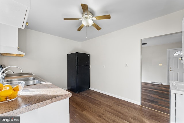 kitchen featuring dark wood-type flooring, black fridge, sink, ceiling fan, and washer / dryer