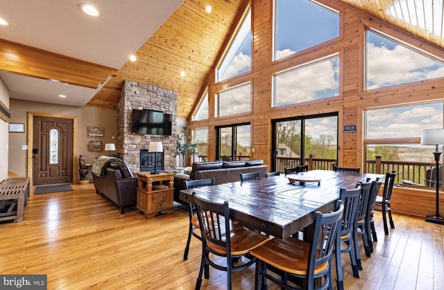 dining room with high vaulted ceiling, wooden walls, a fireplace, wood ceiling, and light wood-type flooring