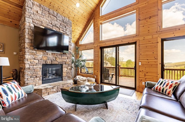 living room with light wood-type flooring, wood ceiling, high vaulted ceiling, a stone fireplace, and wood walls