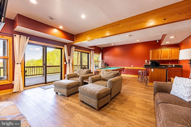 living room with beam ceiling, a textured ceiling, light hardwood / wood-style floors, and pool table