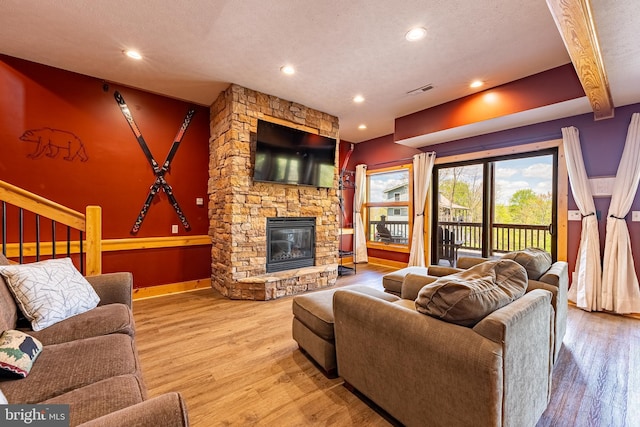 living room featuring hardwood / wood-style flooring, a stone fireplace, and a textured ceiling