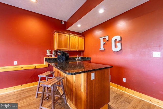 bar featuring light hardwood / wood-style floors, sink, and dark stone counters