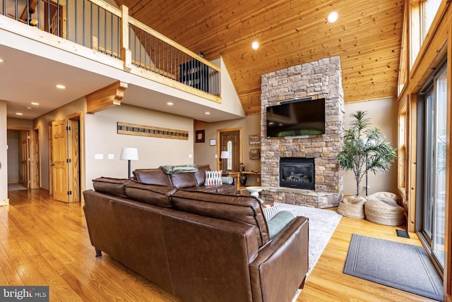 living room with a fireplace, wood ceiling, a high ceiling, and light hardwood / wood-style flooring