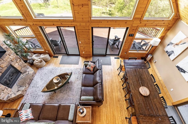 living room with a high ceiling, a stone fireplace, wooden walls, and wood-type flooring