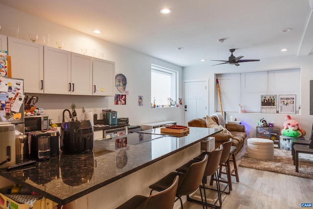 kitchen featuring ceiling fan, a kitchen breakfast bar, dark stone counters, light hardwood / wood-style floors, and white cabinets