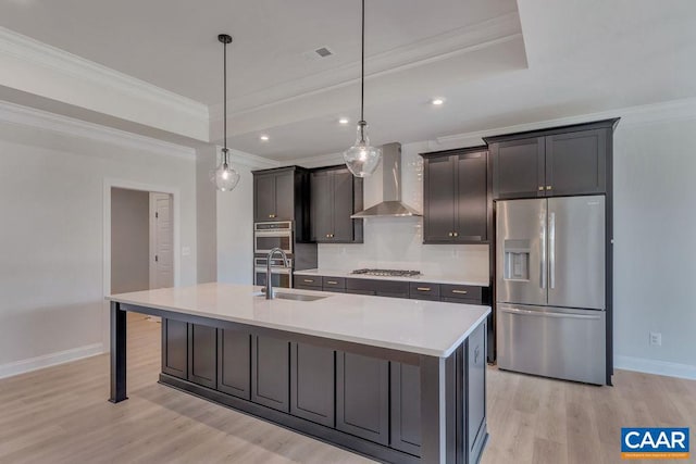 kitchen with pendant lighting, wall chimney range hood, ornamental molding, an island with sink, and appliances with stainless steel finishes