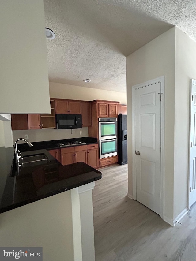 kitchen with light hardwood / wood-style flooring, kitchen peninsula, black appliances, and sink