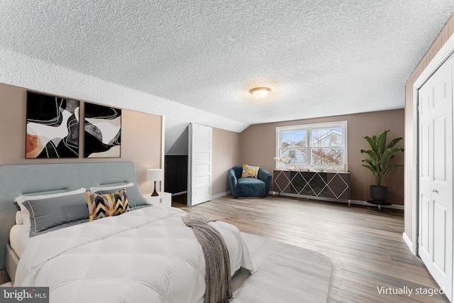 bedroom with a textured ceiling, a closet, wood-type flooring, and lofted ceiling