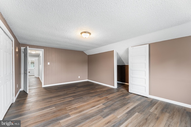 unfurnished bedroom with a textured ceiling, dark hardwood / wood-style flooring, and lofted ceiling