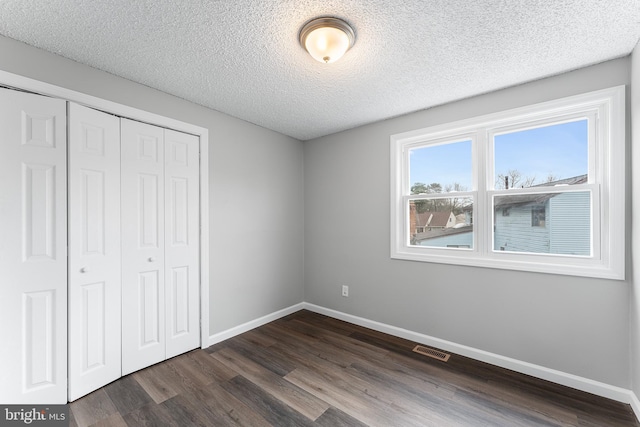 unfurnished bedroom featuring dark hardwood / wood-style flooring, a textured ceiling, and a closet