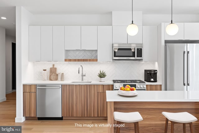 kitchen with pendant lighting, sink, decorative backsplash, white cabinetry, and stainless steel appliances