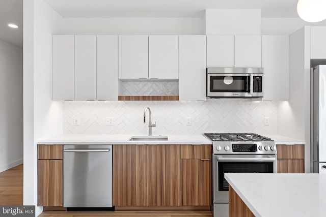 kitchen with decorative backsplash, appliances with stainless steel finishes, sink, light hardwood / wood-style flooring, and white cabinets