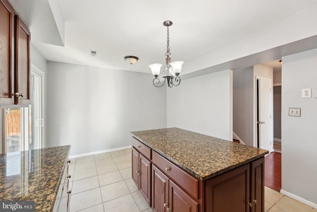 kitchen featuring a kitchen island, dark stone counters, light tile patterned floors, and an inviting chandelier