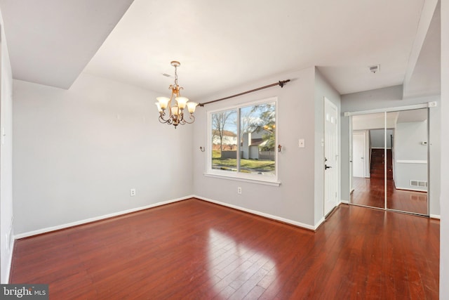 empty room with dark hardwood / wood-style flooring and an inviting chandelier