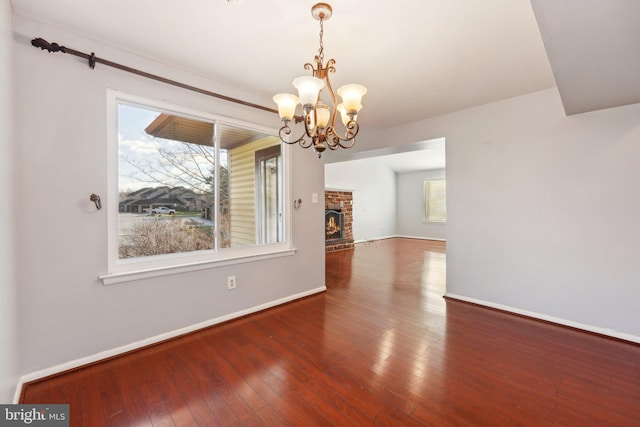 unfurnished dining area with hardwood / wood-style floors, a fireplace, and a chandelier