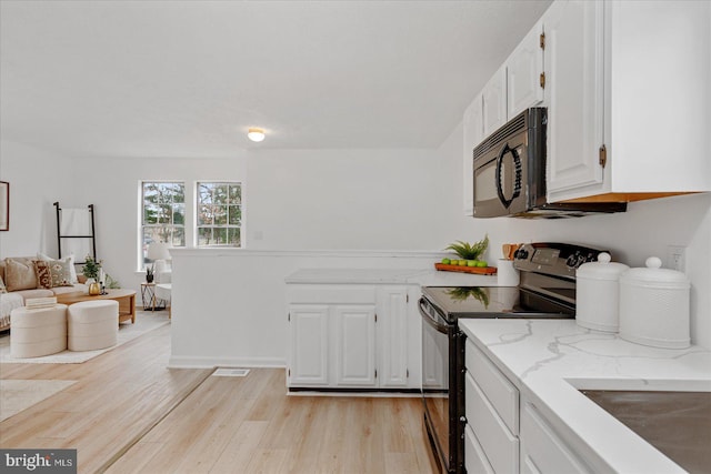 kitchen featuring light stone counters, white cabinets, black appliances, and light hardwood / wood-style floors