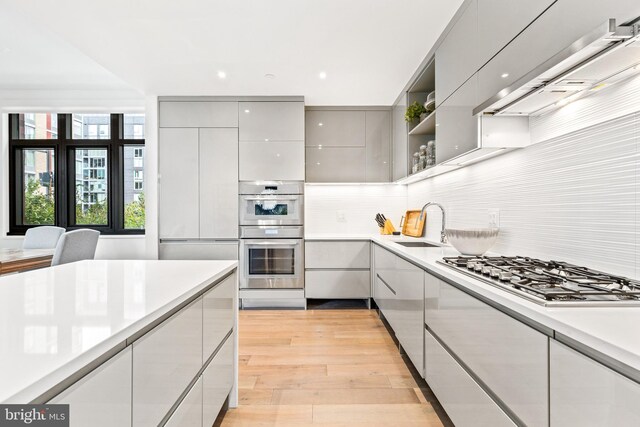 kitchen featuring backsplash, gray cabinetry, stainless steel appliances, sink, and light hardwood / wood-style flooring