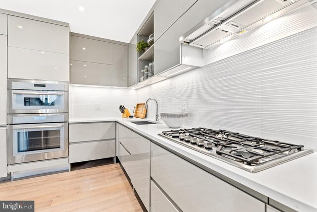 kitchen featuring gray cabinetry, ventilation hood, sink, light wood-type flooring, and stainless steel appliances