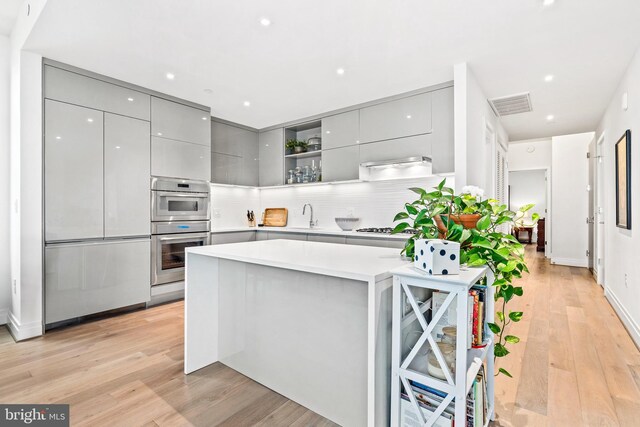 kitchen with gray cabinetry, sink, stainless steel appliances, tasteful backsplash, and light hardwood / wood-style flooring