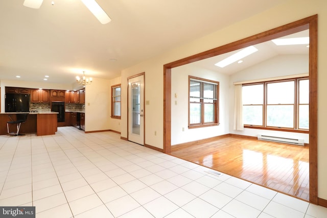 unfurnished living room featuring baseboards, an inviting chandelier, light tile patterned flooring, a baseboard heating unit, and lofted ceiling with skylight