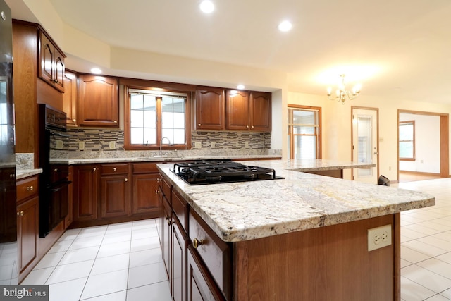 kitchen with light stone counters, an inviting chandelier, a sink, black gas stovetop, and tasteful backsplash