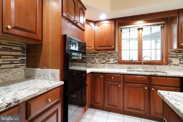 kitchen with dobule oven black, light stone countertops, tasteful backsplash, and a sink