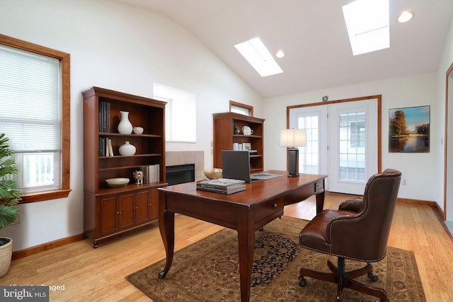office featuring a tiled fireplace, lofted ceiling with skylight, light wood-style floors, and baseboards