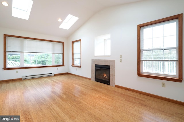 unfurnished living room with a tiled fireplace, vaulted ceiling with skylight, a baseboard heating unit, and light wood-style floors