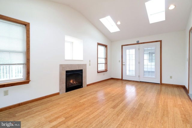unfurnished living room featuring wood finished floors, a fireplace, lofted ceiling with skylight, and a healthy amount of sunlight